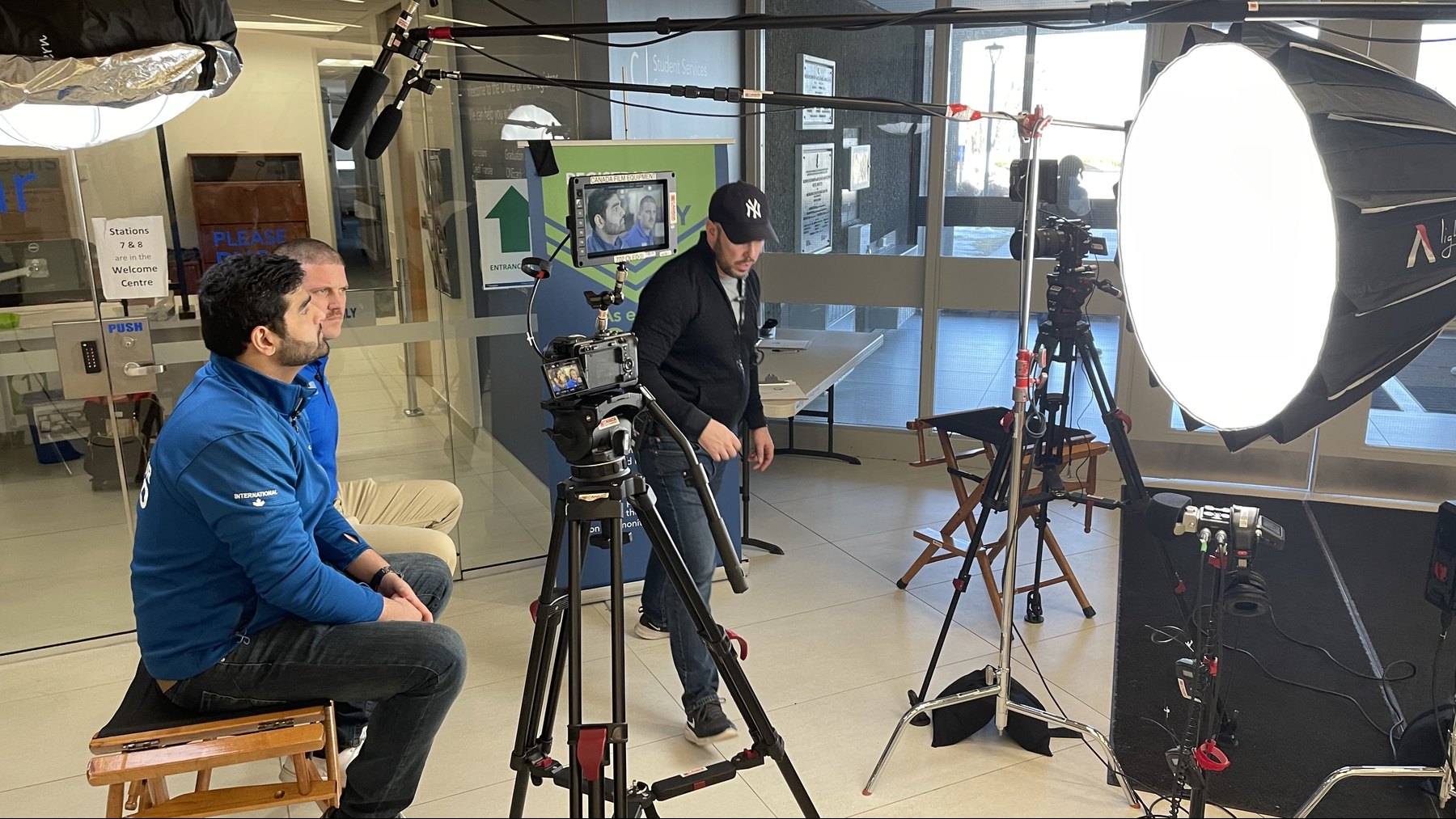 Two interview participants, a crew member and a two-camera setup with lighting and boom microphones