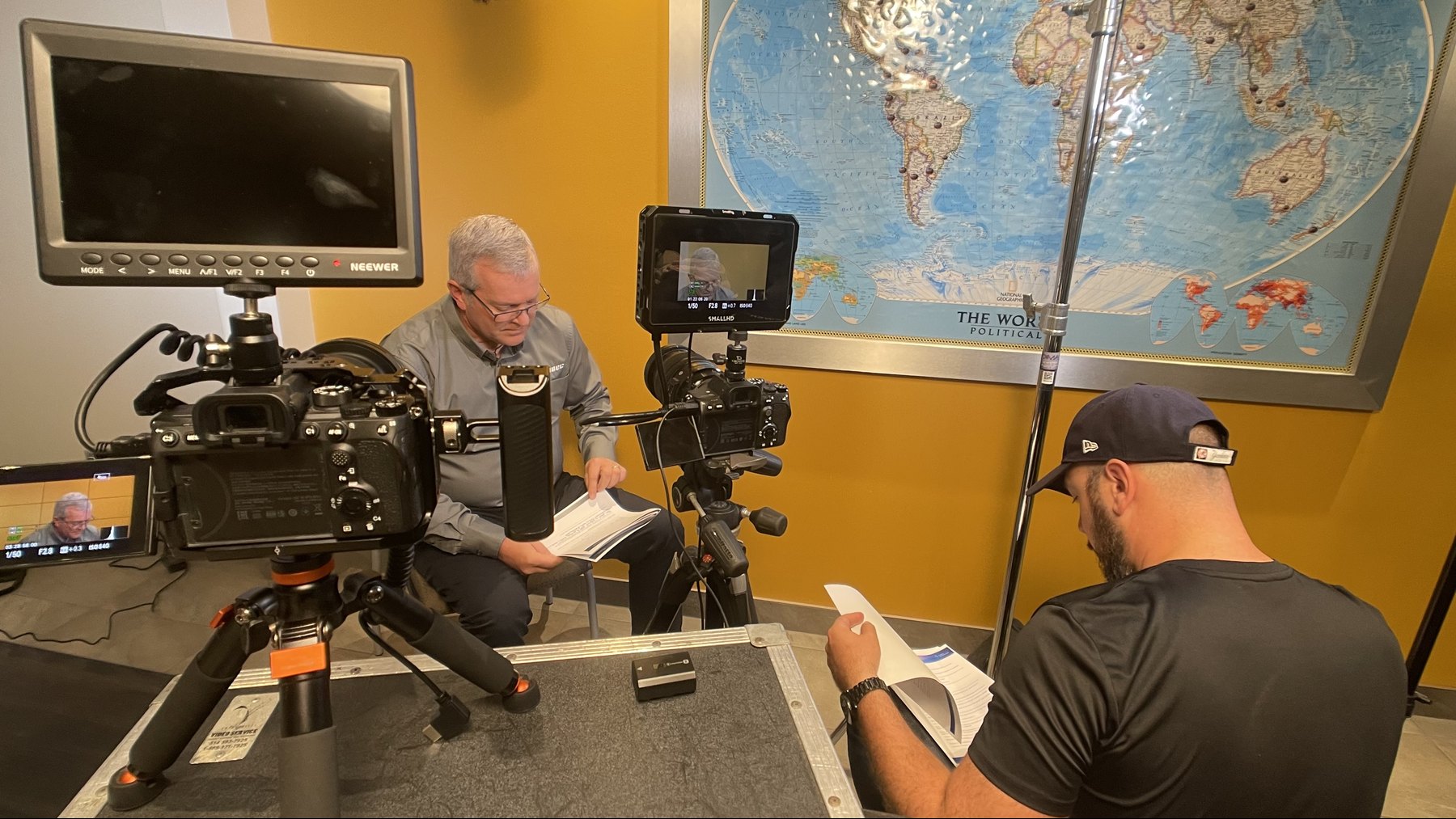 An interview participant and a crew member reviewing printed material beside two cameras